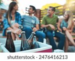 Couple of friends, drinks and backyard party by cooler box for summer celebration and social hangout. People or group relax together with cold beverage, beer or alcohol bottle in ice on patio at home