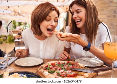 Couple of friends feeding each other with pizza at restaurant. Smiling young woman and her best friend sitting at fast food restaurant and feeding each other a pizza - Powered by Shutterstock