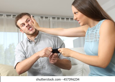 Couple Or Friends Fighting For A Mobile Phone Sitting On A Couch At Home