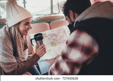 Couple of friends on roadtrip sitting at the back in their camper van. Smiling woman holding coffee and man looking at the map. - Powered by Shutterstock