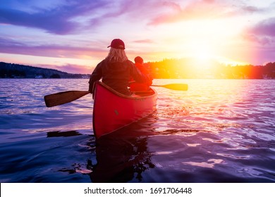 Couple friends on a wooden canoe are paddling in water during a vibrant sunny sunset. Taken in Indian Arm, near Deep Cove, North Vancouver, British Columbia, Canada. Concept: Adventure, Sport, Explore