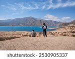 Couple of friends seen from the back, he sitting on the ground and she standing, looking at the landscape in front of the Potrerillos reservoir, in Mendoza, Argentina.