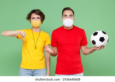 Couple Friends Sport Family Woman Man Football Fans In Face Masks Safe From Coronavirus Virus Covid-19 Cheer Up Support Favorite Team With Soccer Ball Showing Thumb Down Isolated On Green Background
