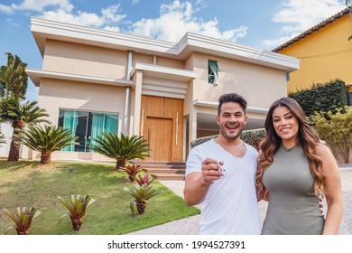 Couple In Front Of New Large Modern House, Outdoors. Happy Couple With Dream House In The Background.