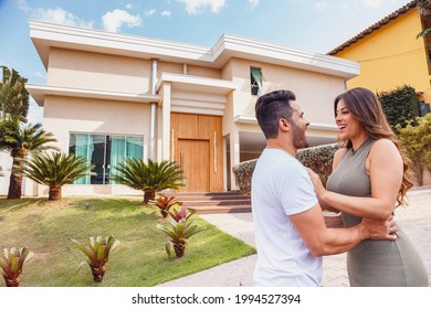 Couple In Front Of New Large Modern House, Outdoors. Happy Couple With Dream House In The Background.