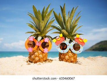 Couple of funny attractive pineapples in children's cheerful sunglasses on sand against turquoise sea. Tropical summer vacation concept. Happy sunny day on the beach of tropical island.  - Shutterstock ID 633460067