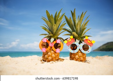 Couple of funny attractive pineapples in children's cheerful sunglasses on sand against turquoise sea. Tropical summer vacation concept. Happy sunny day on the beach of tropical island.  - Shutterstock ID 639817198
