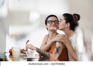 A Couple Of Gay Woman Having Breakfast Together And Holding Hands While Smiling And Kissing. Same Sex Young Married Female Couple In Their Daily Routine At A Morning Showing Some Affection LGBT