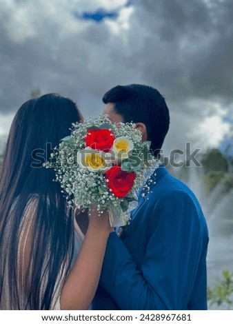 Couple giving each other a passionate and loving kiss, hiding behind the wedding yoke, under an opaque but beautiful sky.