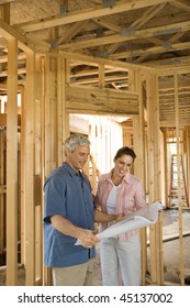 Couple Go Over Home Building Plans At A Construction Site. Vertical Shot.