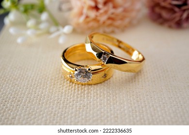 Couple gold wedding rings on a burlap cloth with brown flowers and cream on the back - Shutterstock ID 2222336635