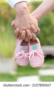 couple hands holding pink baby shoes