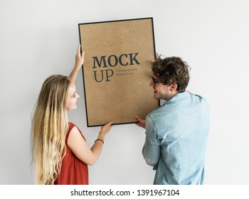 Couple Hanging A Photo Frame Mockup On A White Wall