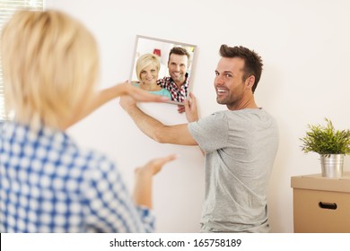 Couple Hanging Photo With Frame On Wall In New Home  