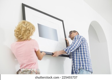 Couple Hanging Picture Frame On Wall In New House