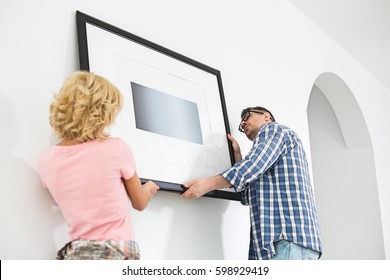 Couple Hanging Picture Frame On Wall In New House