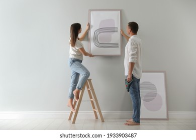 Couple hanging picture on wall together in room. Interior design