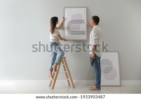 Couple hanging picture on wall together in room. Interior design