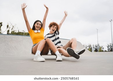 Couple of happy friends teenagers boy girl classmates high school pupils students in colorful t-shirts holding hands up celebration have fun looking at camera in skate ramp park sitting on skateboard - Powered by Shutterstock