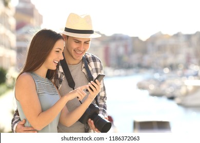 Couple of happy tourists booking hotel online with a smart phone on vacation in a coast town - Powered by Shutterstock