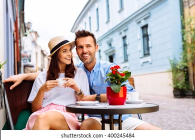 Couple Of Happy Tourists Drinking Coffee On European City Street In Outdoors Cafe