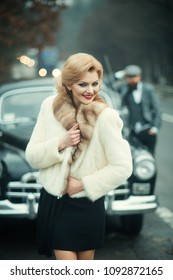 Couple Happy At Vintage Retro Car. Friends On Winter Road Trip In Black Car. Beautiful Young Caucasian Man And Sexy Woman Smiling Joyful In Fur Coat