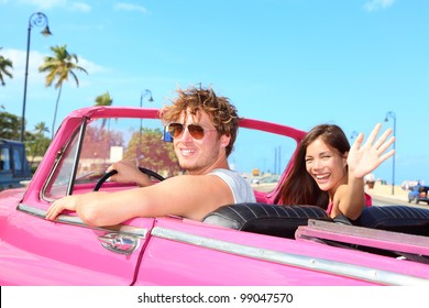 Couple Happy In Vintage Retro Convertible Car. Friends Driving On Summer Road Trip In Pink Car. Beautiful Young Caucasian Man And Asian Woman Smiling Joyful On Sunny Summer Day Traveling.