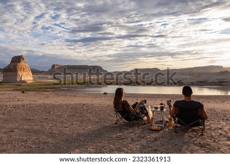 Couple having breakfast at campground with scenic sunrise view of Wahweap Bay at Lake Powell, Glen Canyon Recreation Area, Page, Utah, USA. Vanlife on lone rock beach. Road trip romantic atmosphere