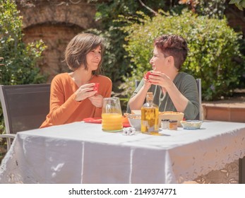 Couple having breakfast outside. There is an lgbt couple of two women having a continental breakfast in a country house on a sunny day. They are dressed casual in green and orange colors. - Powered by Shutterstock