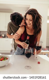 Couple Having Date Night. Man Standing Behind A Woman Filling Wine Glasses In Kitchen. Romantic Couple In The Kitchen With Wine.