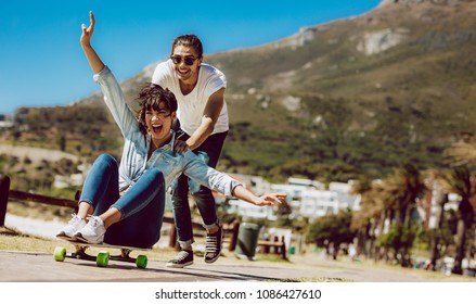 Couple having fun outdoors near the beach. Man pushing her girlfriend on a skateboard. - Powered by Shutterstock