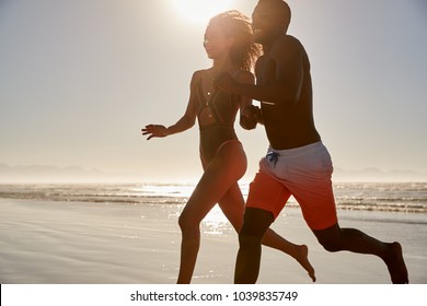 Couple Having Fun Running Through Waves On Beach Vacation