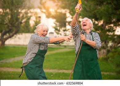 Couple having fun, water hose. Cheerful senior people outdoors. You are never too old.