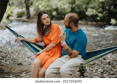 Couple having a heartfelt conversation while sitting on a hammock near a tranquil river amidst lush greenery, enjoying a relaxing moment in nature. - Powered by Shutterstock