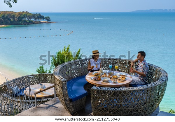 couple having lunch at a restaurant looking\
out over the ocean of Pattaya Thailand, man and woman having dinner\
in a restaurant by the ocean in Pattaya.\
