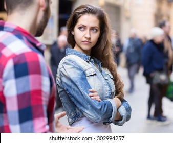 Couple Having A Quarrel On A City Street. Woman Is Standing Half-turned To Her Boyfriend With A Dissapointed Look On Her Beautiful Face