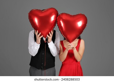 Couple with heart-shaped air balloons for Valentine's day on grey background