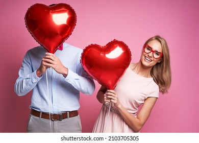 A couple hiding behind a heart shape balloons