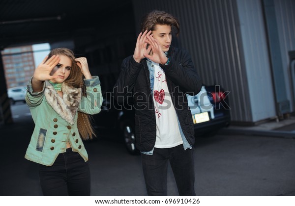 パパラッジの外に顔を隠すカップルが駐車中 ロックスタイルのファッションの若い夫婦 写真家に顔を隠す美しい少女とハンサムな男性 の写真素材 今すぐ編集
