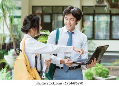 A Couple Of High School Students Standing Wearing A Bag While Using A Laptop Computer Together With Finger Pointing To Screen