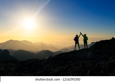 Couple hikers celebrating success in sunset mountains, accomplish with arms up outstretched. Young man and woman looking at beautiful inspirational landscape view, Gran Canaria Canary Islands.