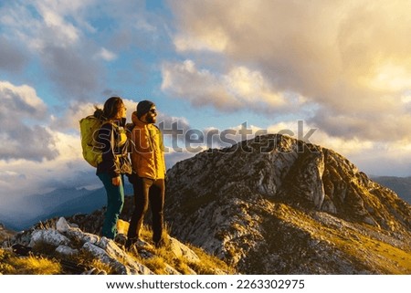 a couple of hikers equipped with mountain equipment, warm clothes and a backpack on top of a mountain watching the sunset. Mountaineers perform exercise in the mountains. sport and outdoor adventure.