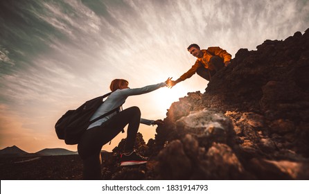 Couple of hikers helping each other climbing a mountain at sunset. People giving a helping hand and active sport concept.