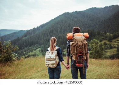 A couple hikers Hiking with backpacks walk along a beautiful mountain area holding hands . The concept of active rest
