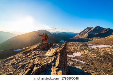 Couple of hikers looking at view from mountain top against sun burst. Man and woman on vacation in scenic alpine landscape, summer activities fitness wellbeing freedom