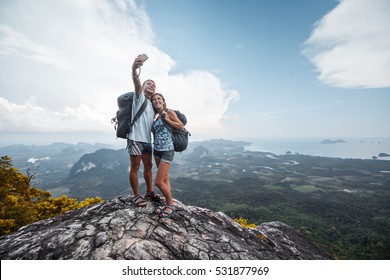Couple of hikers taking selfie from top of the mountain with valley view on the background