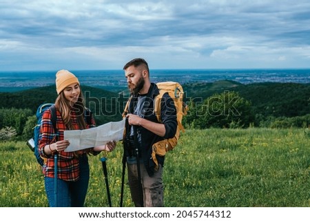 Couple of hikers using trekking poles and a map for orientation while spending time in the nature