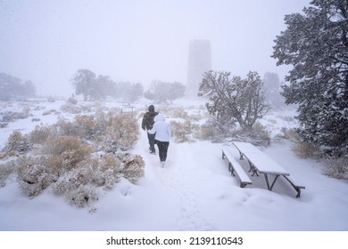 Couple Hiking In Snow Storm On Winter Vacation. People Walking To The Desert View Watchtower. Grand Canyon National Park, Arizona, USA. 