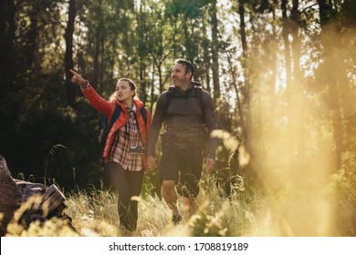 Couple hiking through forest trails. Woman showing something to man while walking towards their camping site. - Powered by Shutterstock