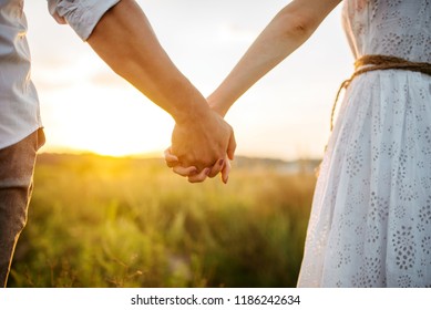 Couple hold hands in green field on sunset - Shutterstock ID 1186242634
